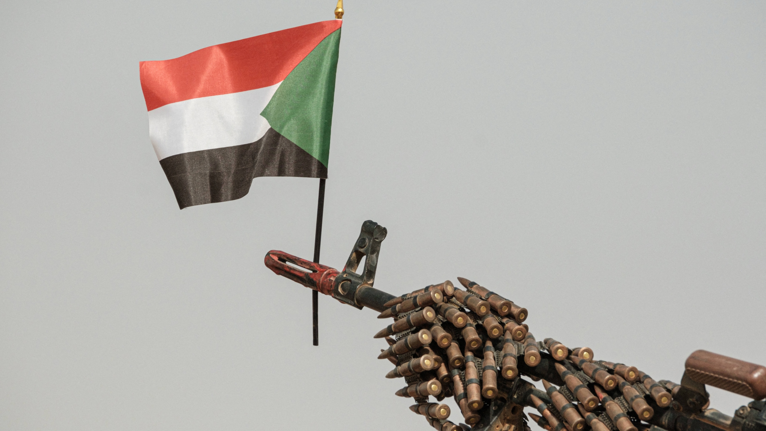 A Sudanese flag placed above the muzzle of a machine gun covered with an ammunition belt of the Rapid Support Forces (RSF) paramilitaries before a rally for supporters in northwest of Khartoum on 22 June 2019 (AFP)