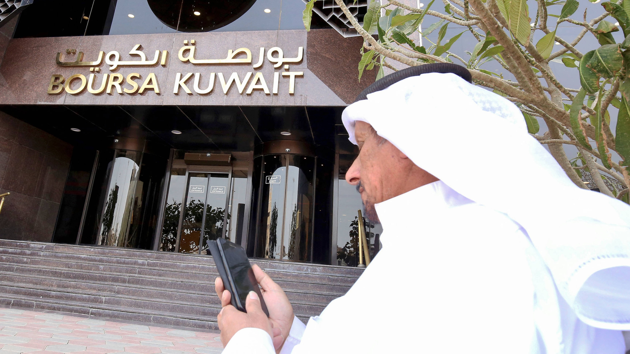 A Kuwaiti trader checks his phone at the entrance of the Boursa Kuwait financial market in Kuwait City, on 8 March 2020 (AFP)