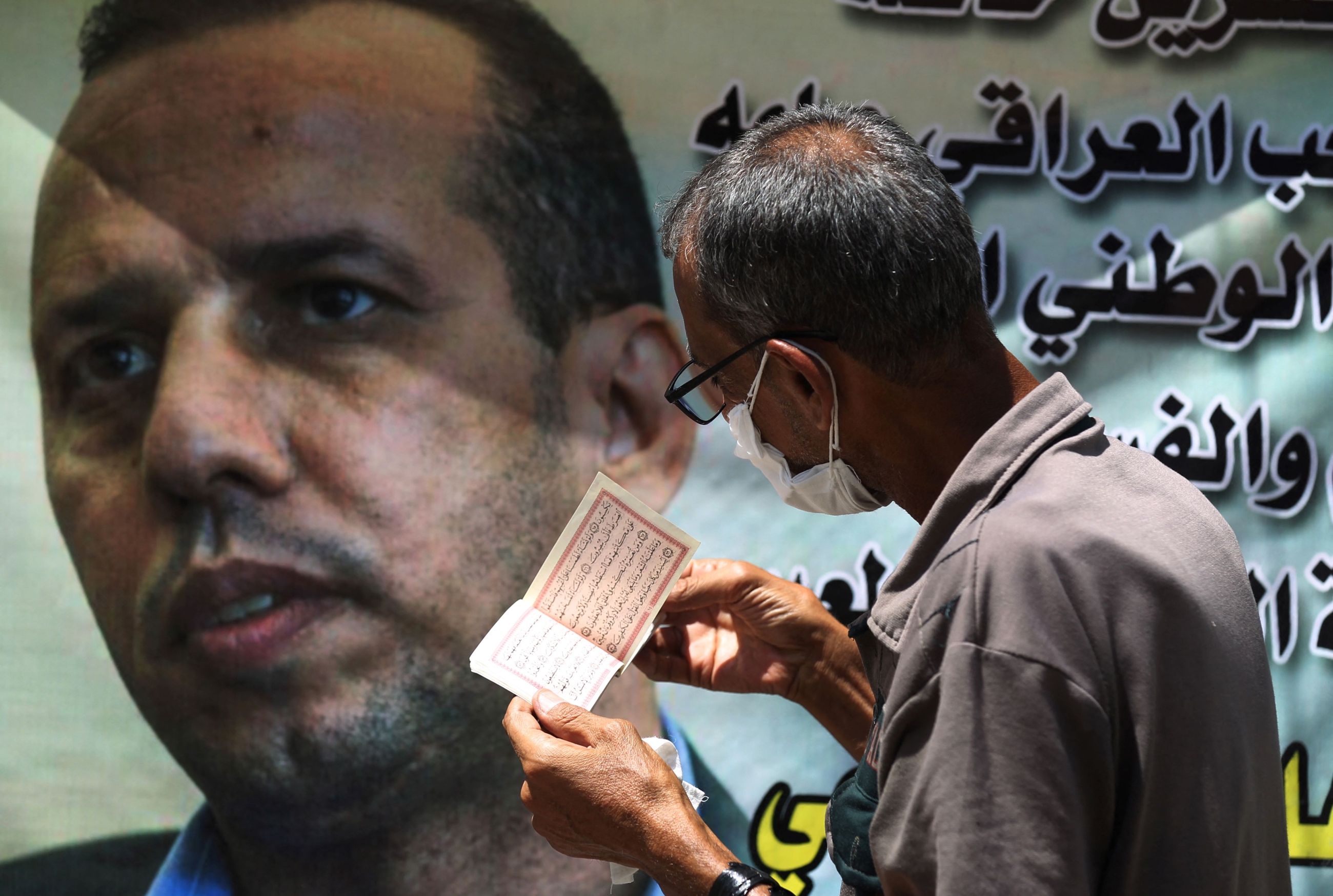An Iraqi man recites verses from the Koran next to a poster of Iraqi jihadism expert Hisham al-Hashemi, who was shot dead outside his house in the Iraqi capital last week, during a protest in the capital Baghdad on July 12, 2020 to demand a curb on paramilitary groups and restricting the use of weapons to government security forces (AFP)