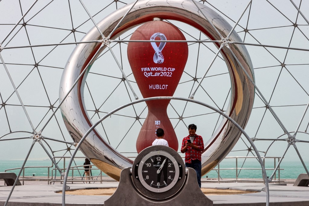 People stand by the clock installation ticking the days to the start of the Qatar 2022 FIFA World Cup, along the waterfront in Qatar's capital Doha during a heavy dust storm on May 17, 2022 as the skyline behind is obscured in the haze. (AFP)