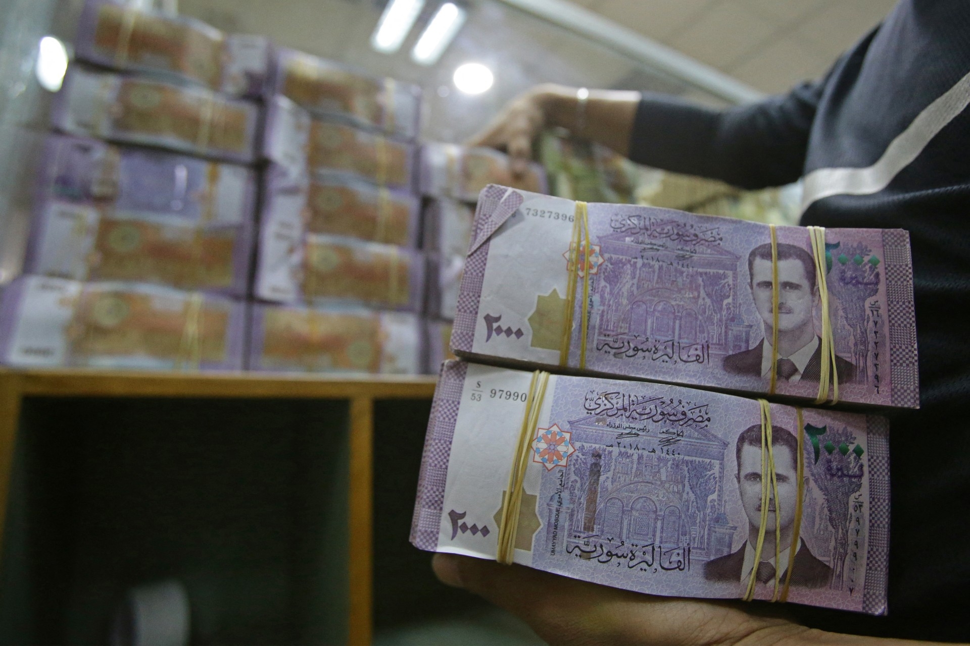 An employee piles up stacks of Syrian lira banknotes at the Commercial Bank of Syria in Damascus (AFP)