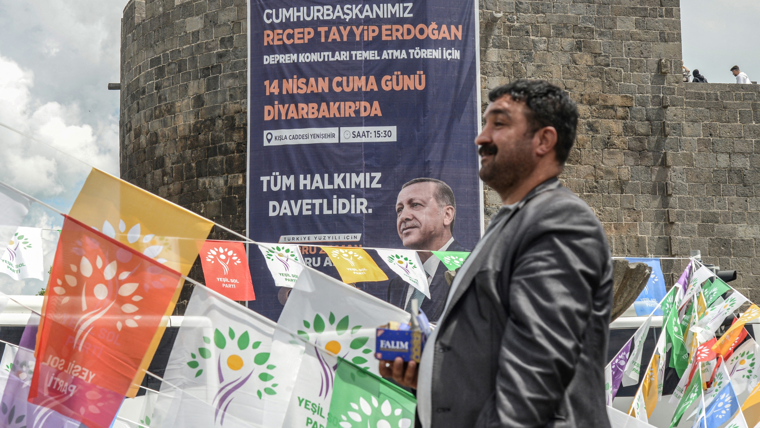 A man walks past election campaign flags of the HDP and a banner with a portrait of Turkish President Recep Tayyip Erdogan hanging on historical Sur castle in Diyarbakir on 1 May 2023 (Reuters)