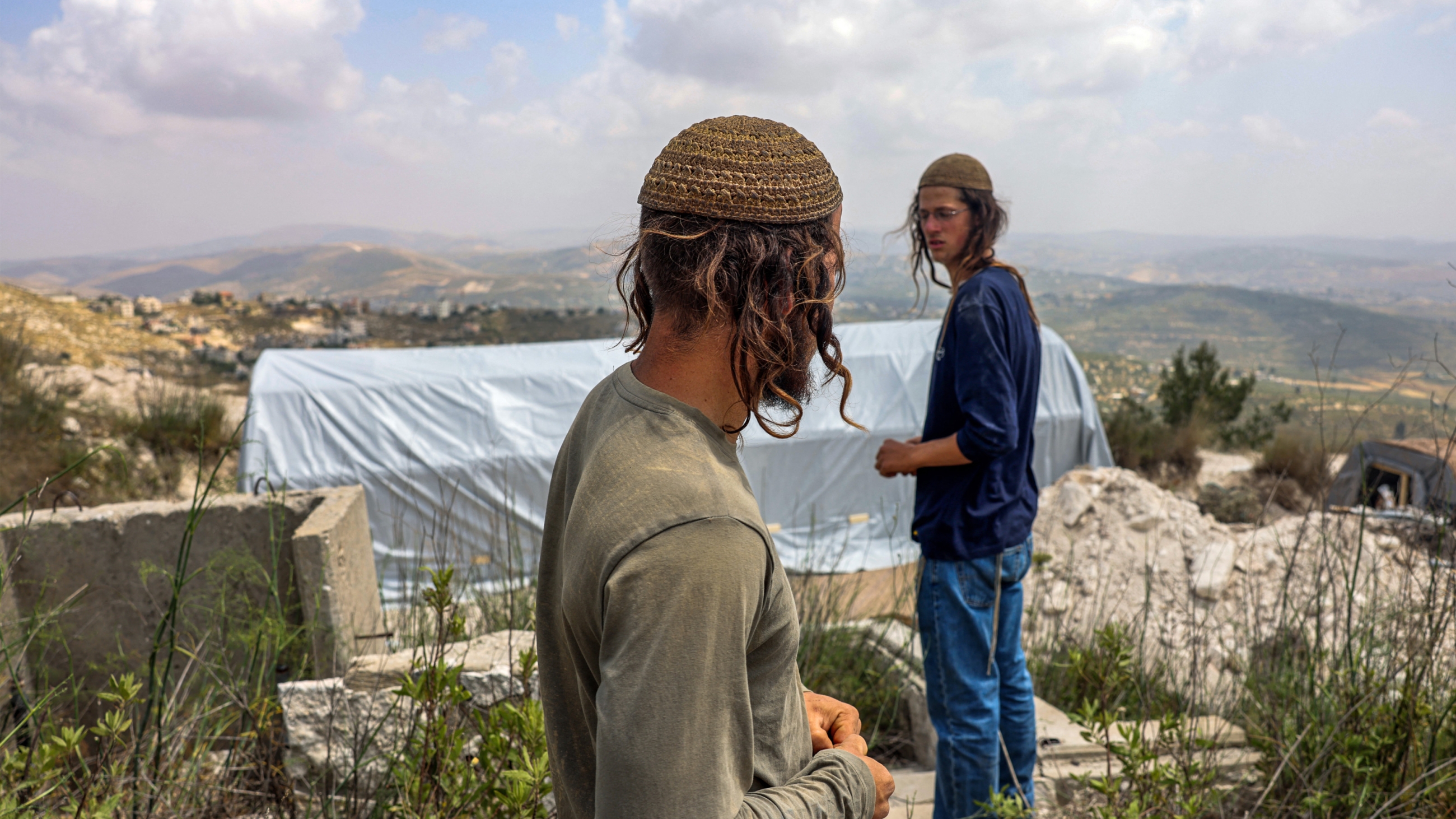 Israeli settlers walk outside a tent at the outpost of Homesh in the occupied West Bank on 29 May 2023 (AFP)