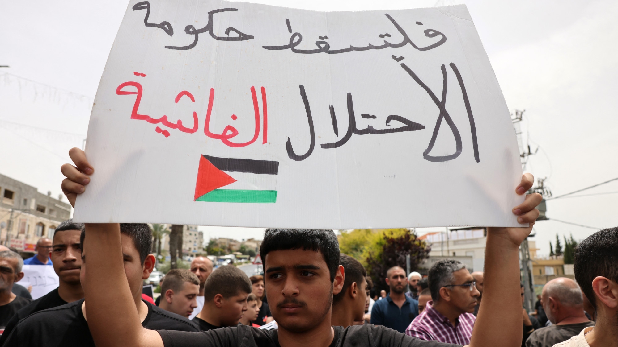 A demonstrator raises a placard that reads 'down with the fascist occupation government' during a protest in the village of Yafia, west of Nazareth, on 9 June 2023 (AFP) 