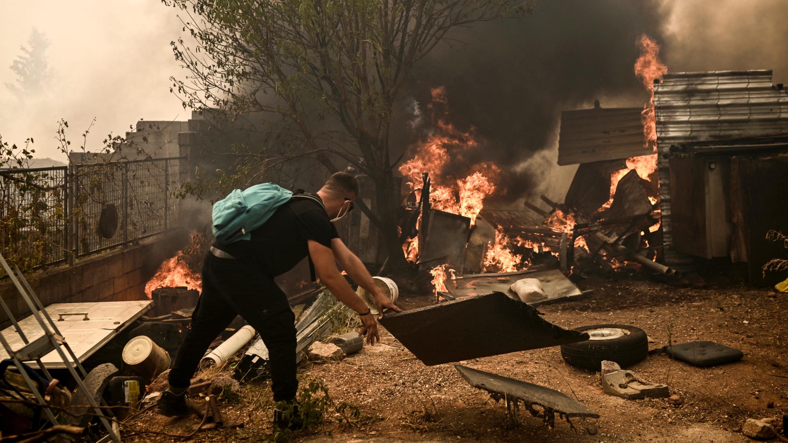 A local resident removes pieces of wood as a wildfire spreads near a house in Acharnes, north of Athens, on 23 August 2023 (AFP)