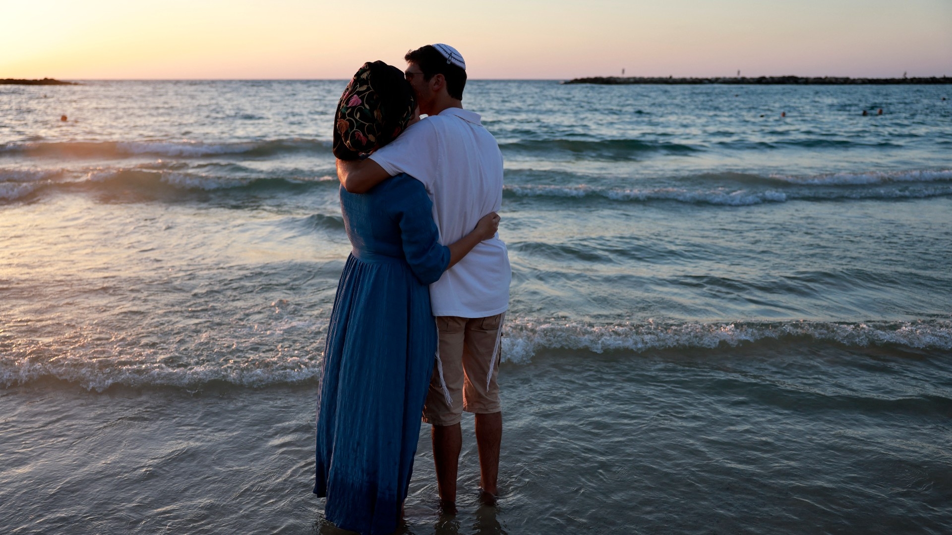 A man and a woman stand along the Mediterranean sea shore as religious Jews gather to perform the Tashlich ritual in Tel Aviv on 17 September ahead of Yom Kippur (AFP)