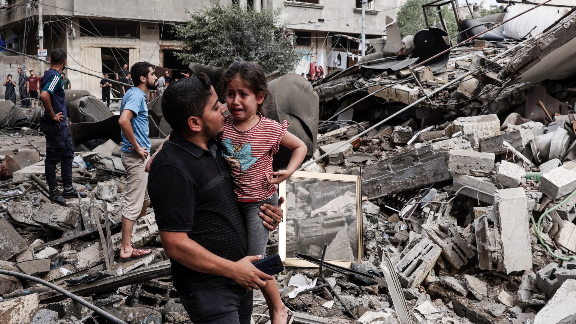 A man carries a crying child as he walks in front of a building destroyed in an Israeli air strike in Gaza City (AFP)