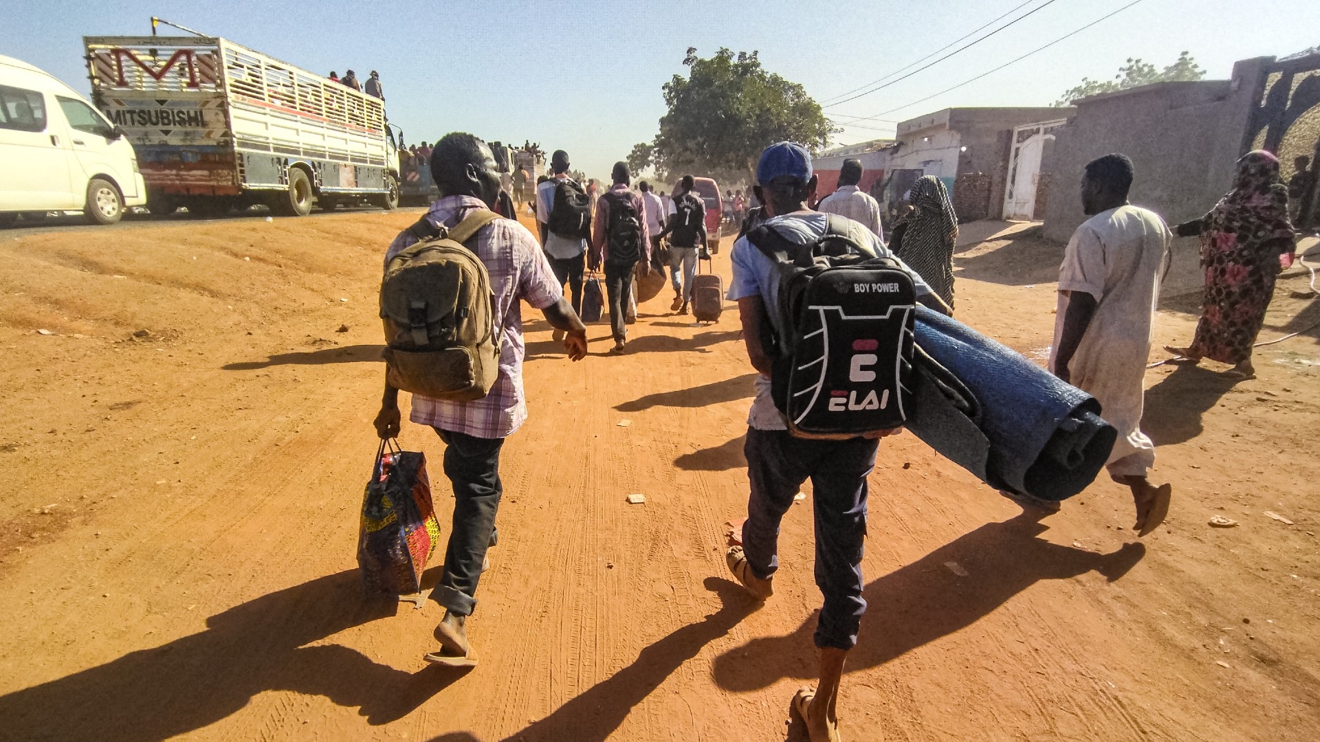 People displaced by the conflict in Sudan walk with their belonging along a road in Wad Madani on 16 December (AFP)
