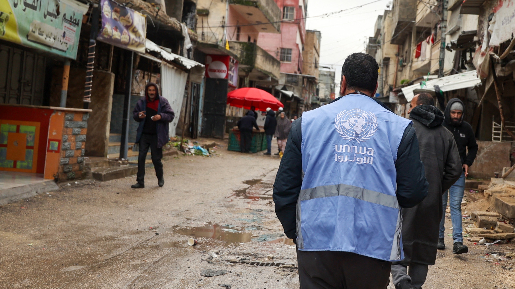 A man wearing a jacket bearing the logo of the United Nations Relief and Works Agency for Palestine Refugees (UNRWA), walks along a street devastated by the passage of Israeli military vehicles and bulldozers during raids, in the refugee camp of Balata in the occupied West Bank on 4 February 2024 (AFP/Jaafar Ashtiyeh)