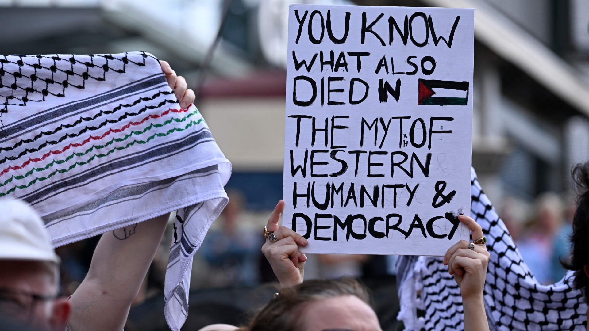 Pro-Palestinian demonstrators protesting against Israel's war in Gaza hold up keffiyeh scarves and a poster during a rally on 8 June in Duisburg, western Germany (Ina Fassbender/AFP)