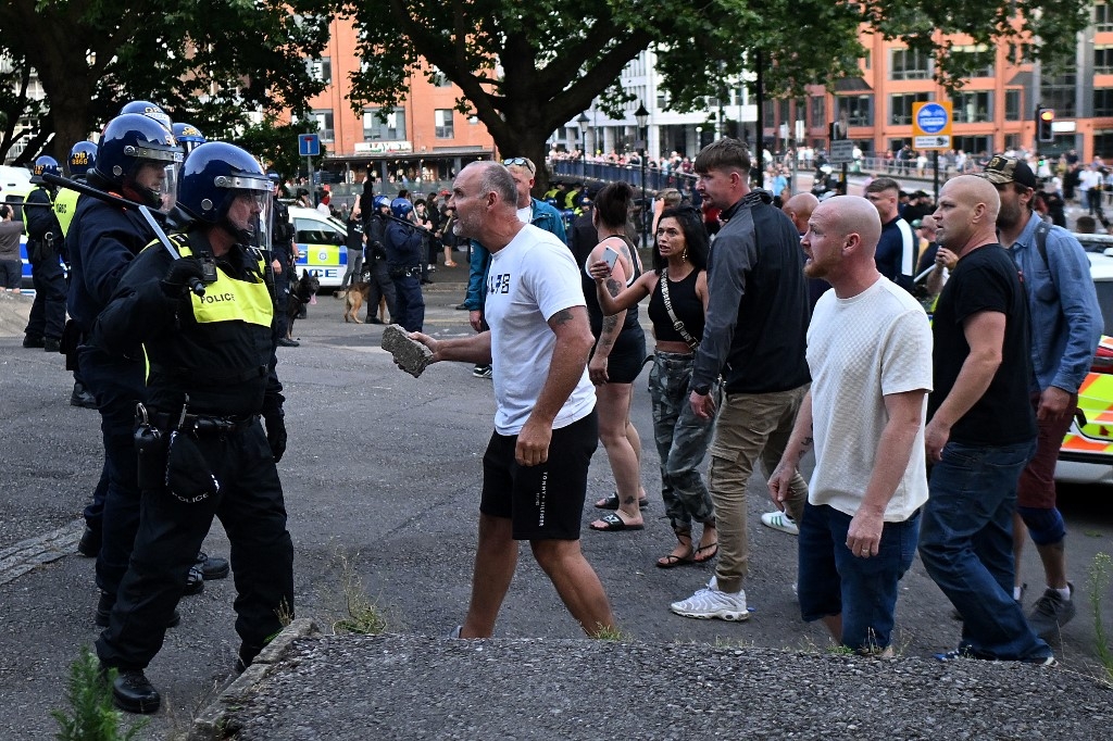 A protester holding a piece of concrete walks towards riot police as clashes erupt in Bristol on August 3 2024 (AFP)