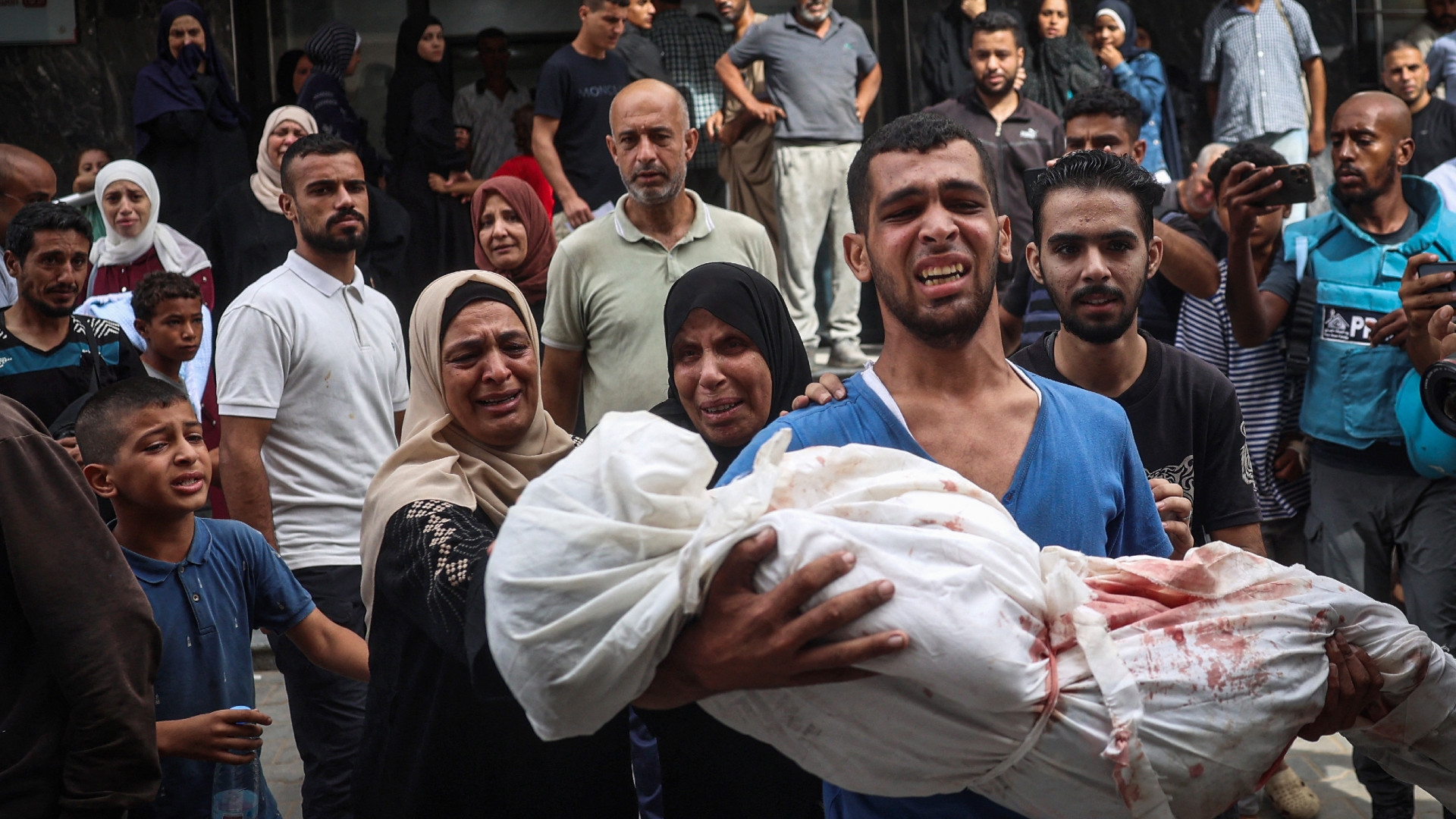 A Palestinian man carries the body of a child killed in Israeli strikes on the Bureij refugee camp, at the al-Awda Hospital at the Nuseirat refugee Camp in central Gaza on 17 September (Eyad Baba/AFP)