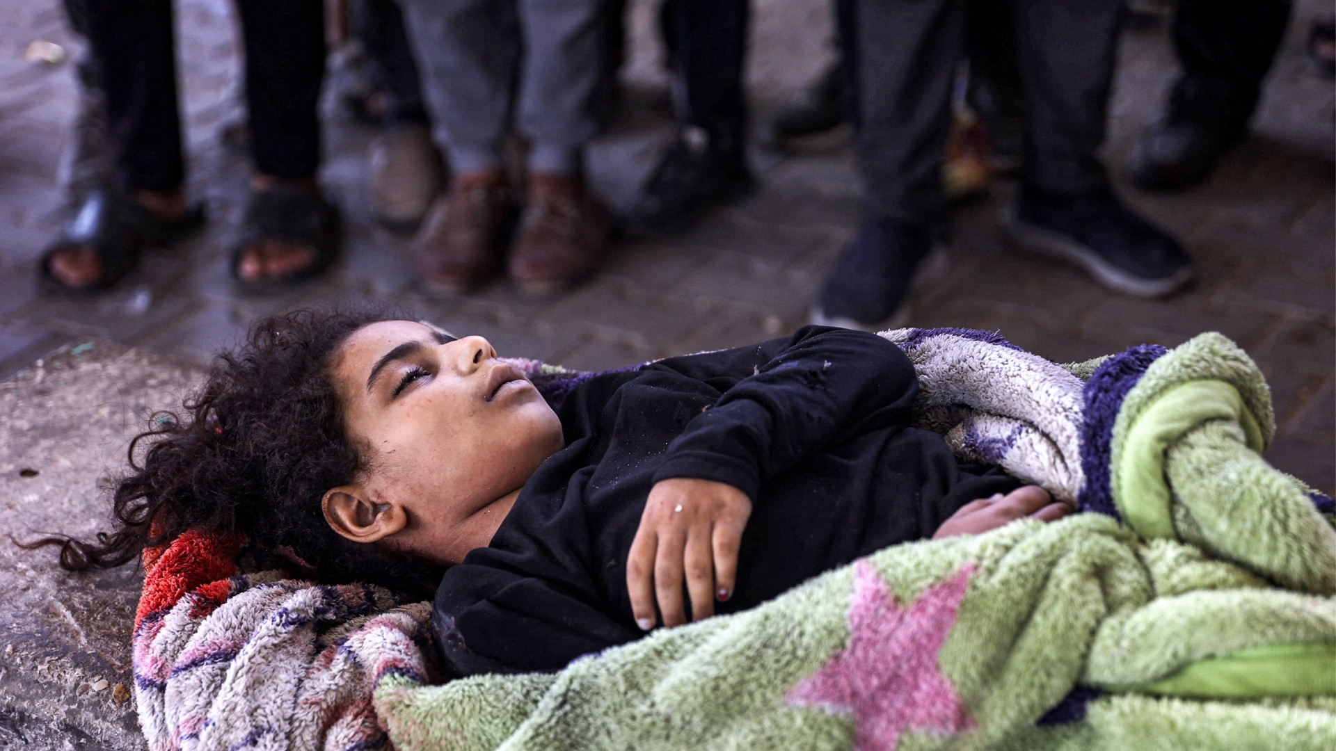 People stand before the body of a girl who was killed during Israel's bombardment of the Rafei school, which served as a displacement shelter in the Jabalia camp for Palestinian refugees in the northern Gaza Strip on 9 October 2024 (Omar Al-Qattaa/AFP)