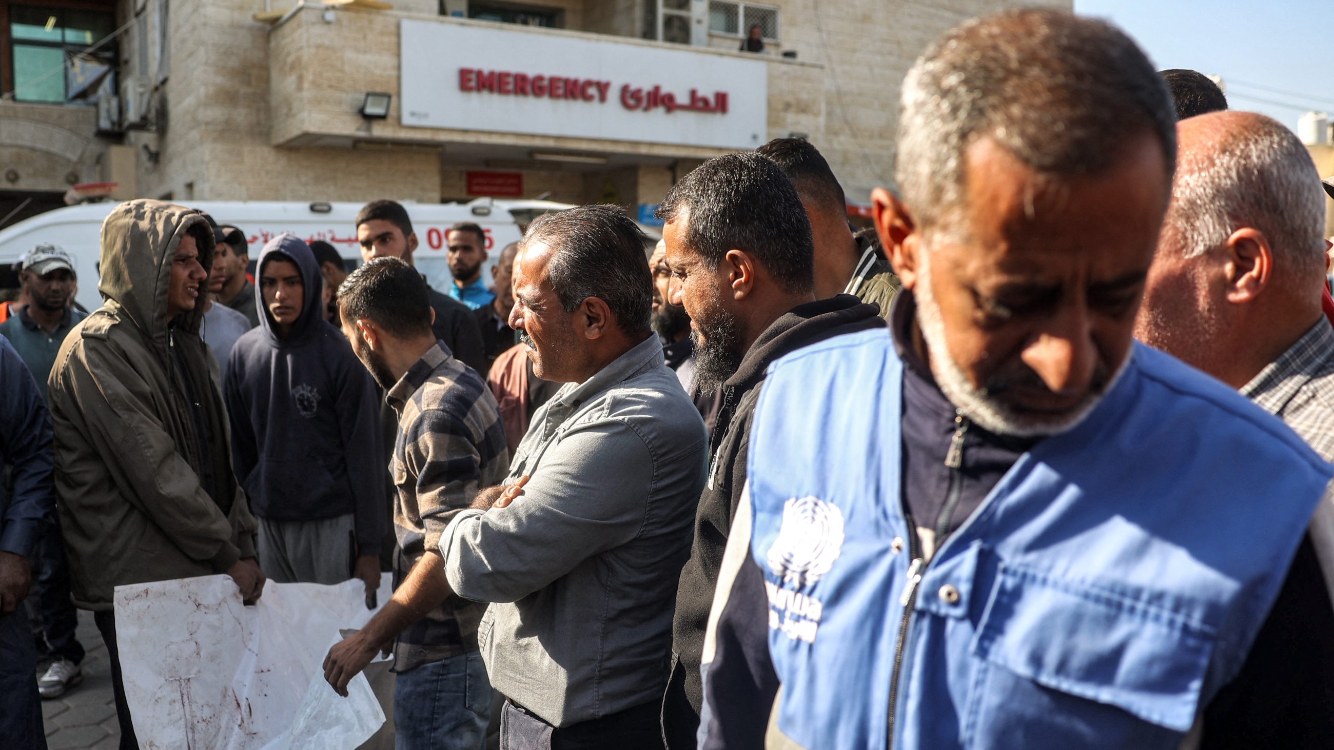 A man wearing an Unrwa vest reacts as people carry one of the bodies of Unrwa workers who were killed when Israeli strikes hit their truck on 23 October (AFP)