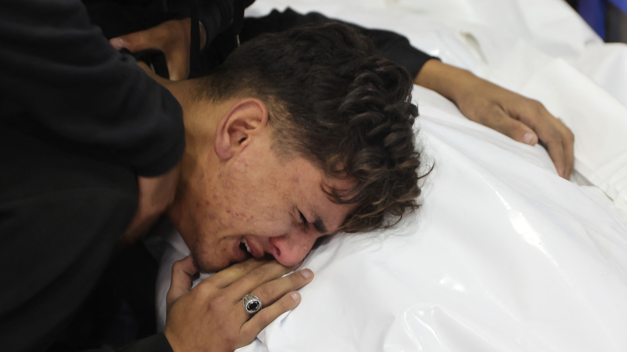 A youth mourns by the covered body of a relative killed in an Israeli strike that destroyed a house on al-Jalaa street in central Gaza City on 18 November 2024 (AFP/Omar al-Qattaa)