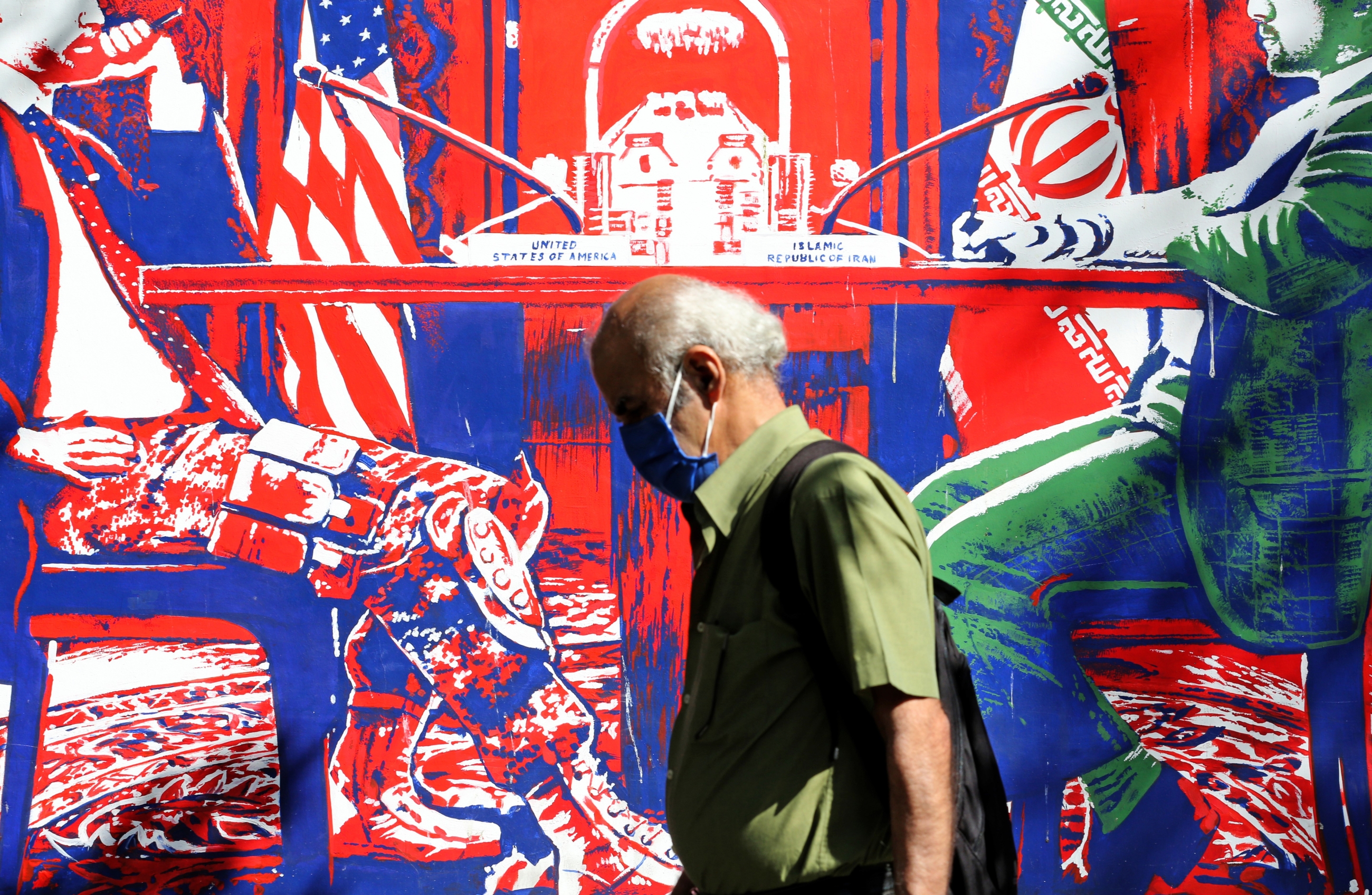 Un homme portant un masque passe devant une fresque peinte sur les murs d’enceinte de l’ancienne ambassade américaine à Téhéran, le 20 septembre (AFP)