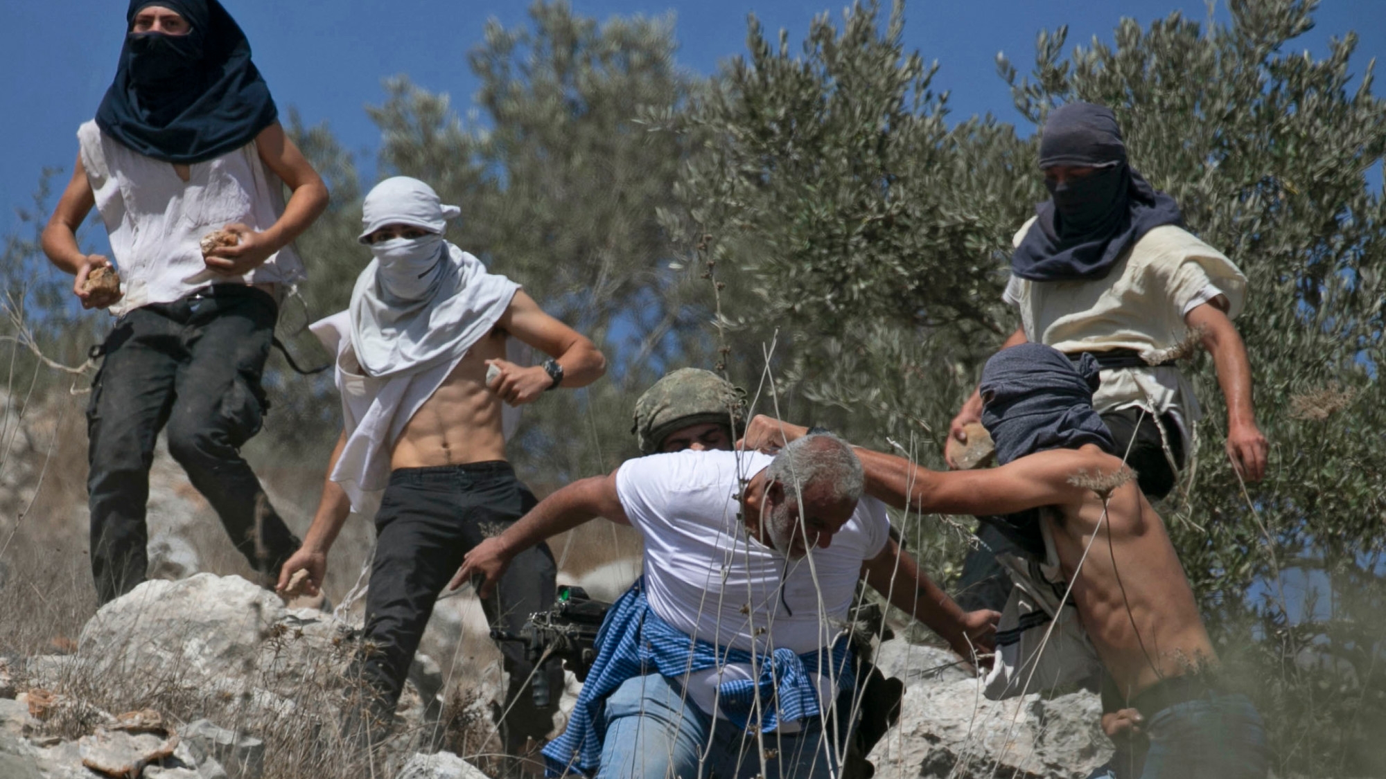 Masked Israeli settlers attack Palestinian olive farmers from the village of Hawara on fields near the settlement of Yitzhar in the occupied West Bank, on 7 October 2020 (AFP/FILE/Jaafar Ashtiyeh)