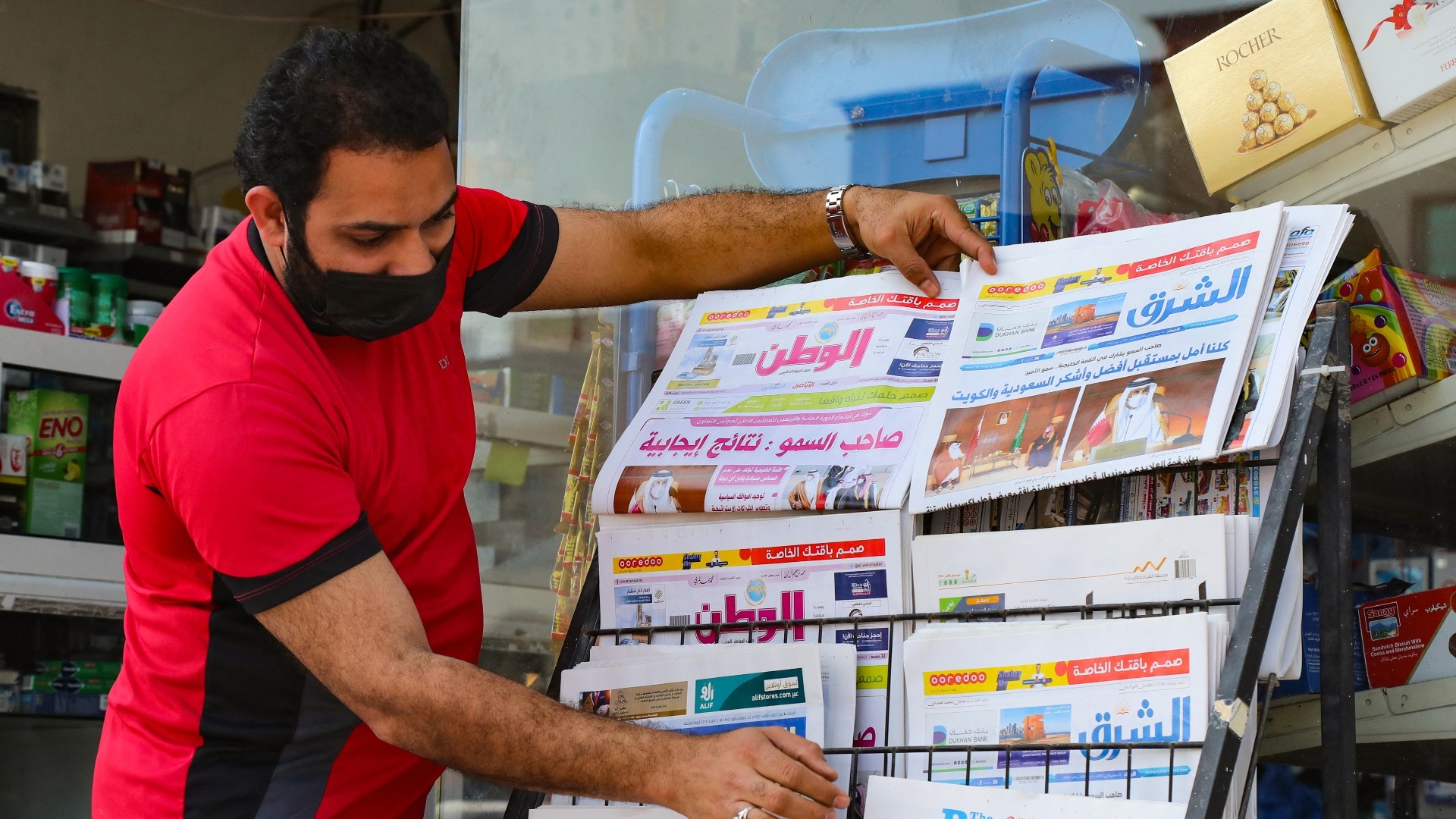 A man arranges newspapers on a stand outside a shop in Doha showing headlines about the summit in al-Ula in 2021, which saw Qatar's relations restored with other Gulf states (AFP)