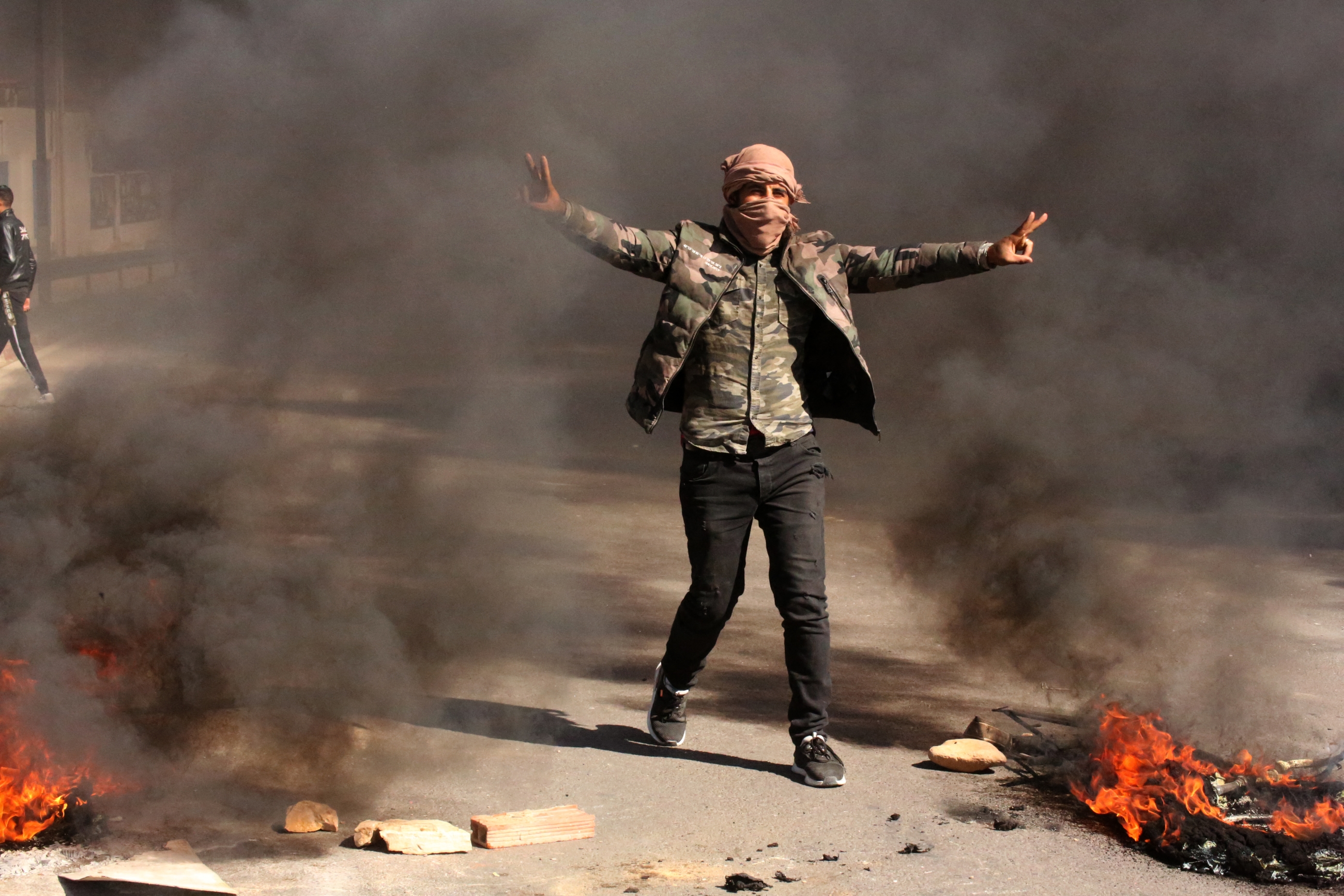 Un Tunisien fait le V comme signe de victoire alors que des jeunes brûlent des pneus et bloquent des routes dans la ville de Tataouine, au sud du pays, le 12 février 2021 (AFP)
