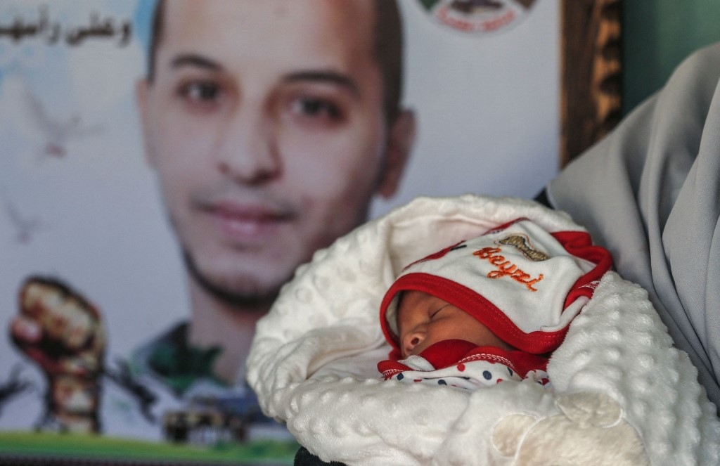 Imane Al-Qudra tient son bébé devant le portrait de son mari, détenu dans une prison israélienne (AFP)