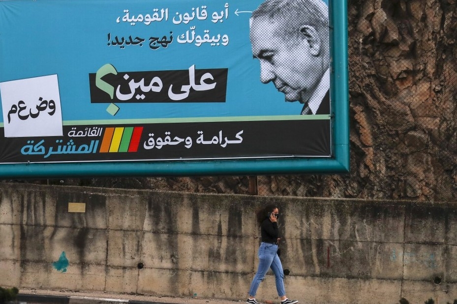 A women walks past an electoral billboard by the Joint List depicting Benjamin Netanyahu with a slogan reading in Arabic "the father of the nation-state law, says "a new approach", whom is he fooling? " in the northern city of Nazareth ahead of the March 2021 election. (AFP)