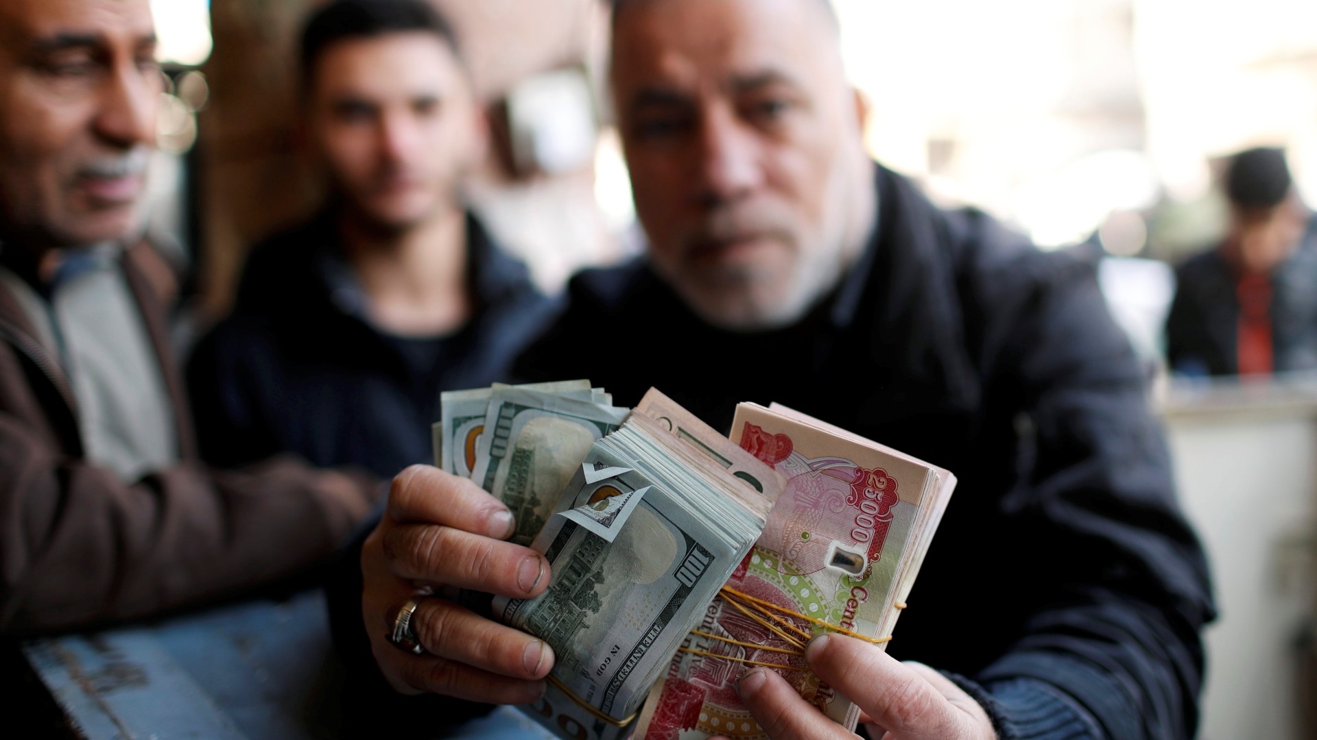 A man holds money as he poses for a picture at a foreign currency exchange market in Baghdad, December 2020 (Reuters)