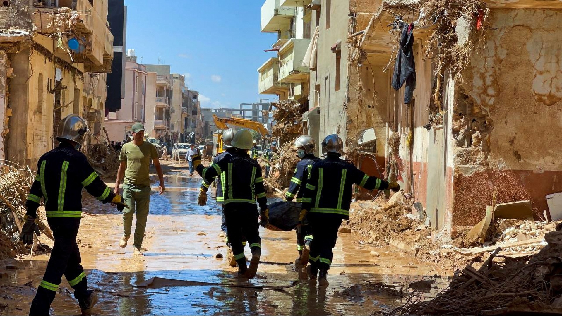 Members of the rescue teams from the Egyptian army carry a dead body as they walk in the mud between the destroyed buildings of Derna, 13 September (Reuters)