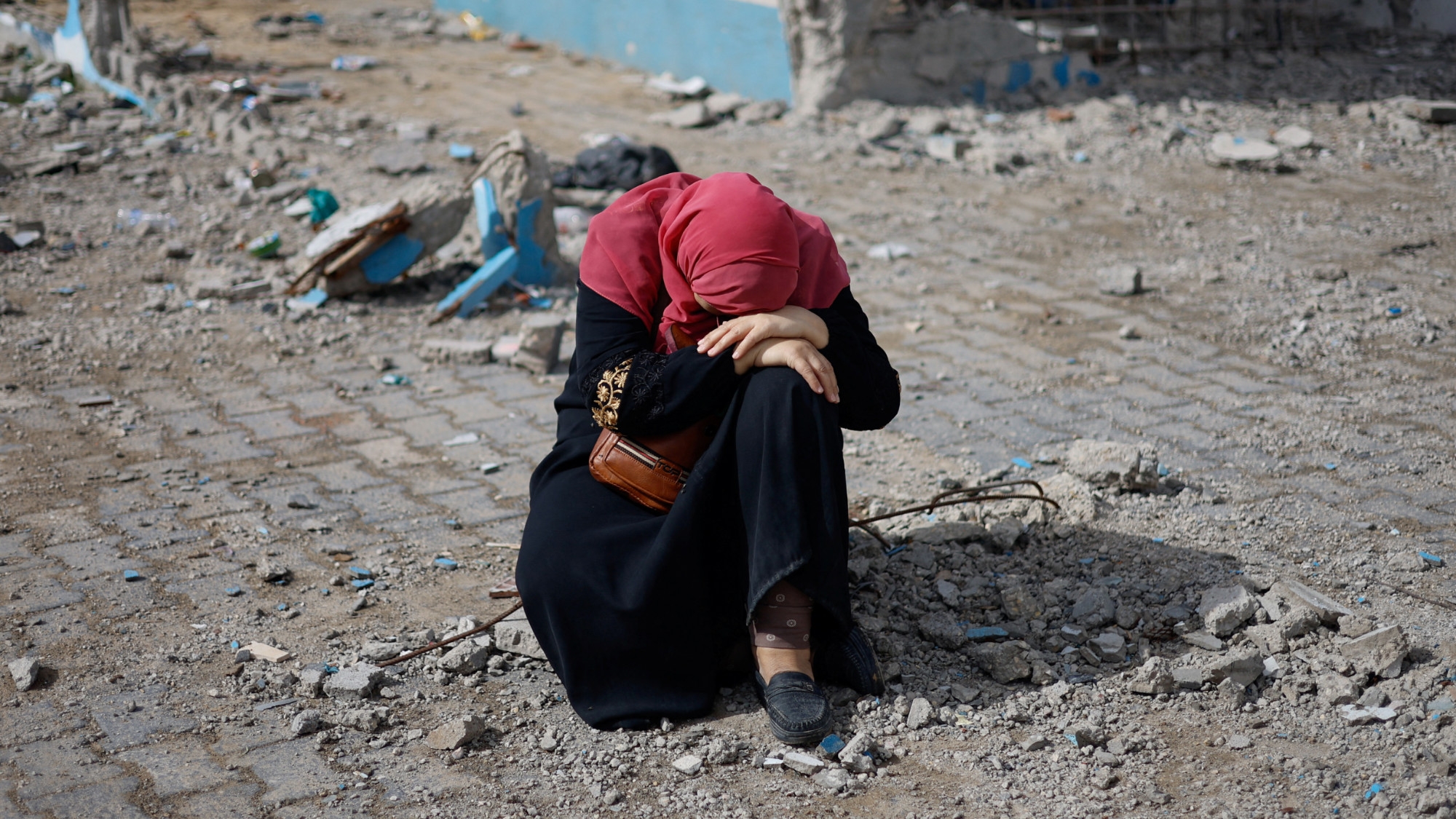A woman rests next to a damaged building in the southern Gaza Strip, 15 February 2024 (Reuters/Mohammed Salem)