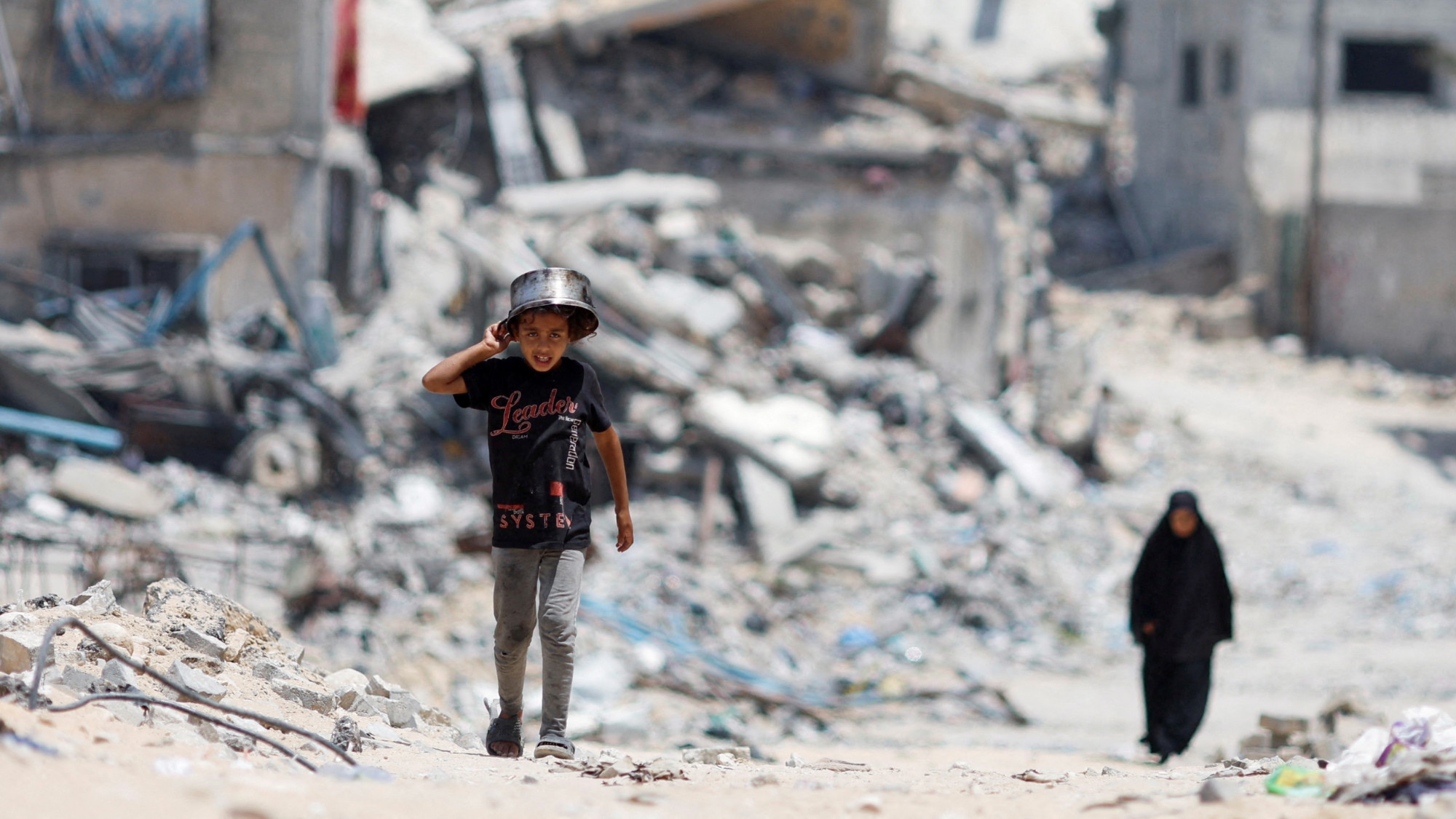 Palestinians walk by houses that were destroyed in an Israeli strike in Khan Younis, in the southern Gaza Strip, 22 May 2024 (Reuters/Mohammed Salem)