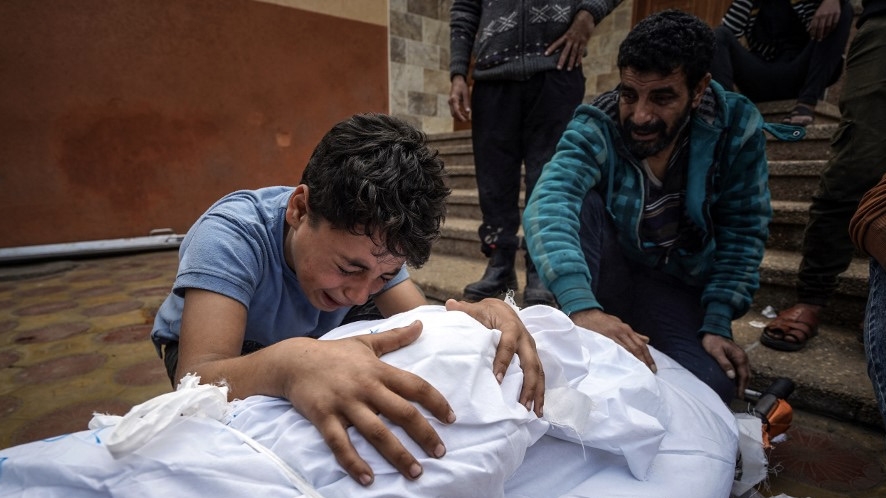 A Palestinian mourns over the body of a relative killed in an Israeli strike at the Nasser hospital in Khan Younis, southern Gaza Strip, 28 December 2023 (AFP)