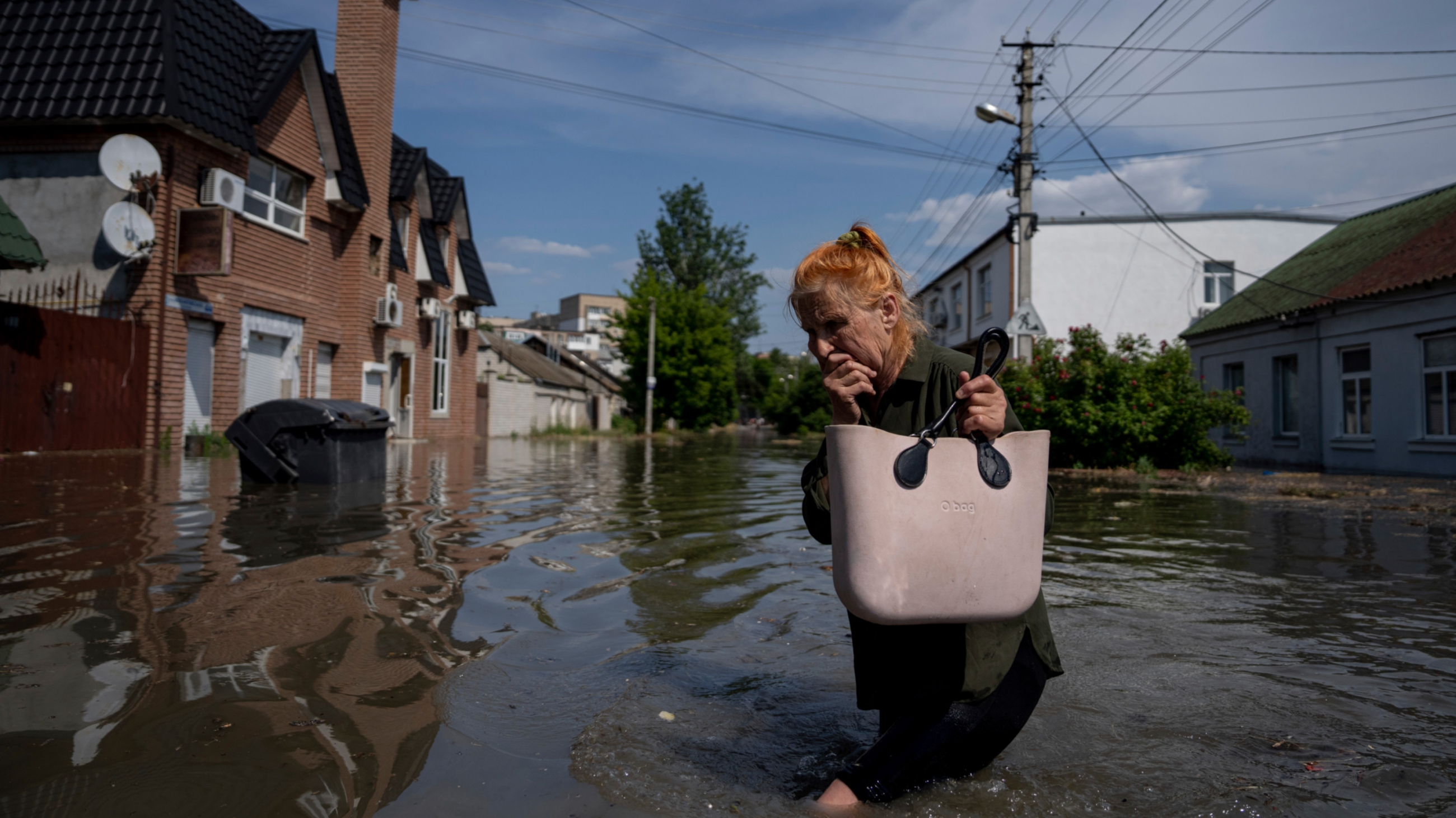 A local resident makes her way through a flooded road after the walls of the Kakhovka dam collapsed overnight in Kherson, Ukraine, 6 June 2023 (AP)