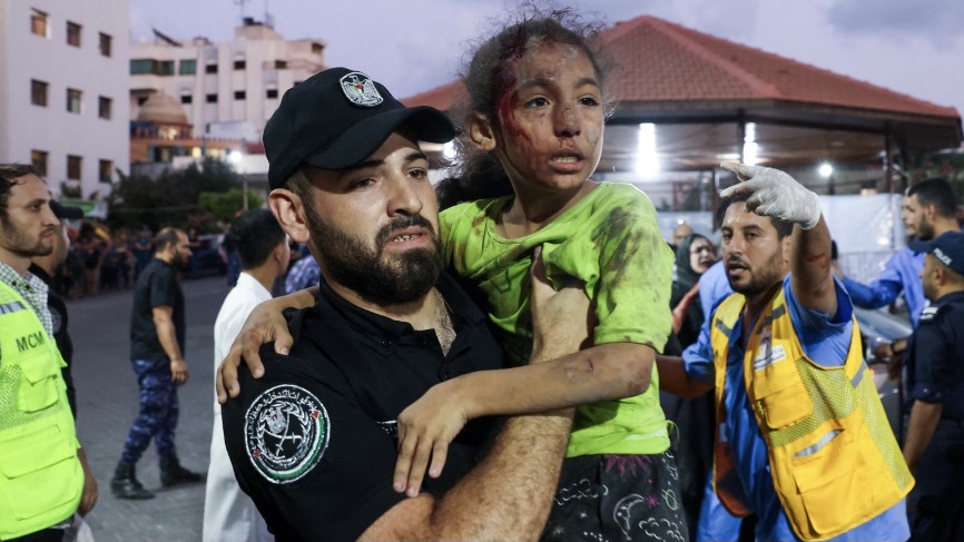A member of the Palestinian security forces carries a child, wounded by Israeli airstrikes, into Al-Shifa hospital in Gaza City on 11 October 2023 (AFP)