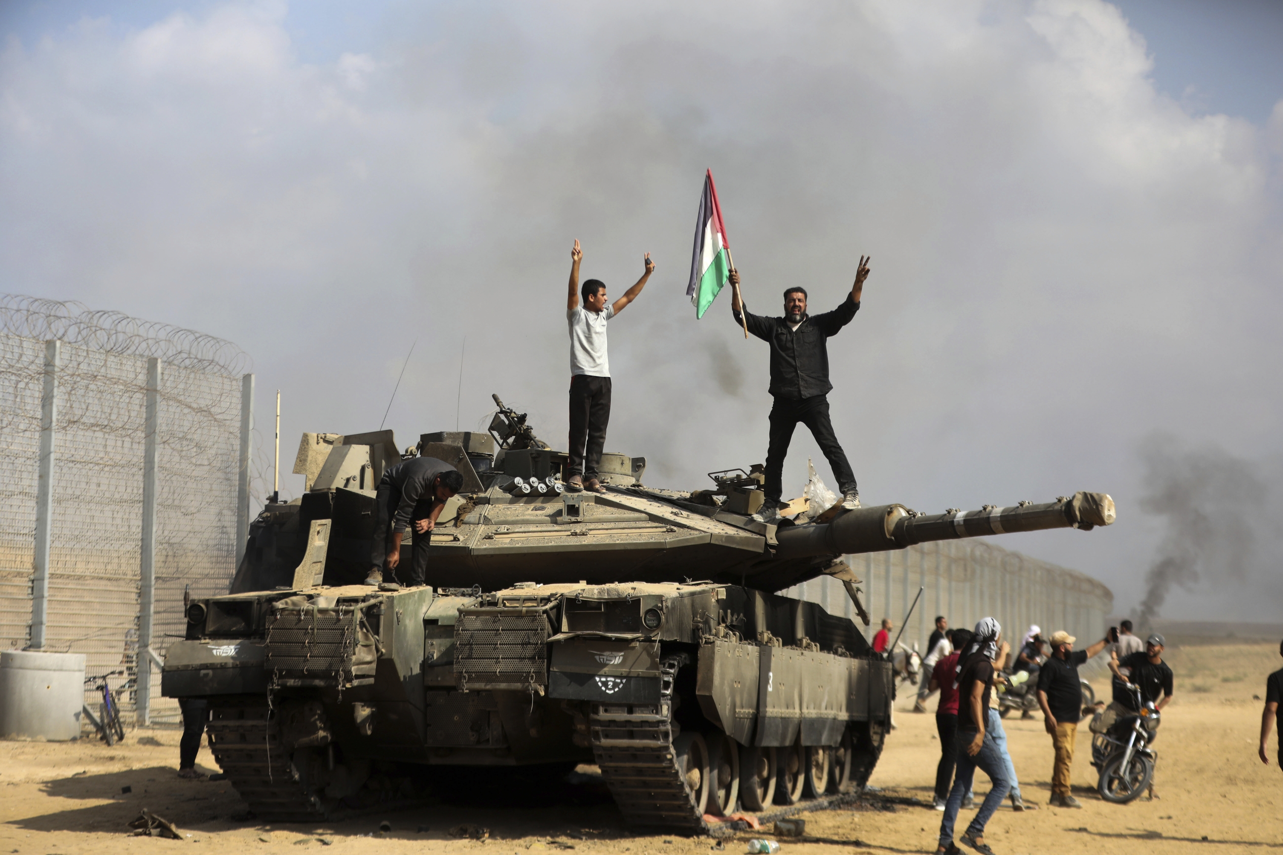 Des Palestiniens brandissent leur drapeau national et se réjouissent sur un tank israélien détruit à la barrière avec la bande de Gaza, à l’est de Khan Younès, le 7 octobre 2023 (AP)
