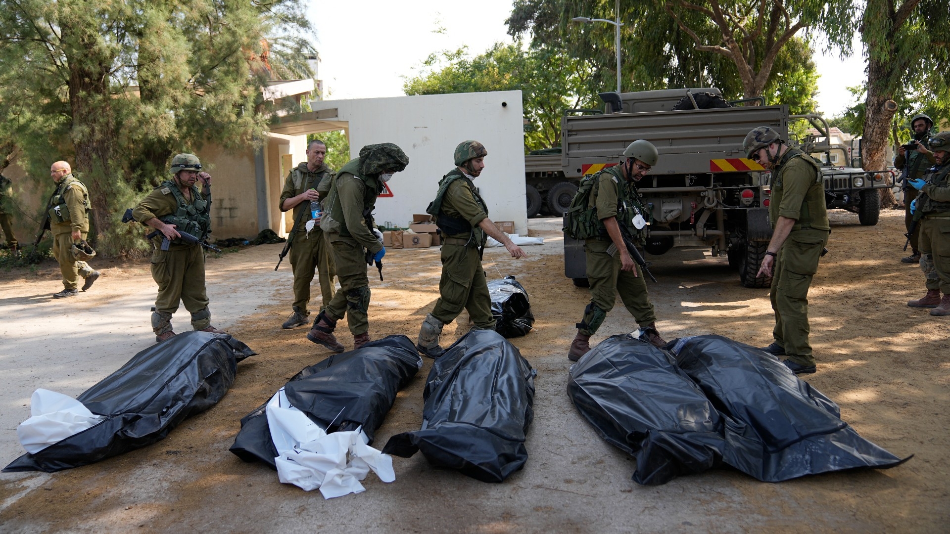 Israeli soldiers stand next to the bodies of Israelis killed by Palestinian fighters in kibbutz Kfar Azza on 10 October (AP)