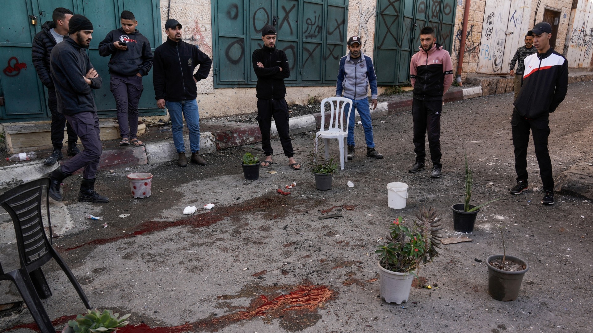 Palestinians look at a blood stain at the site of the Israeli drone strike in Jenin, 12 December (AP)