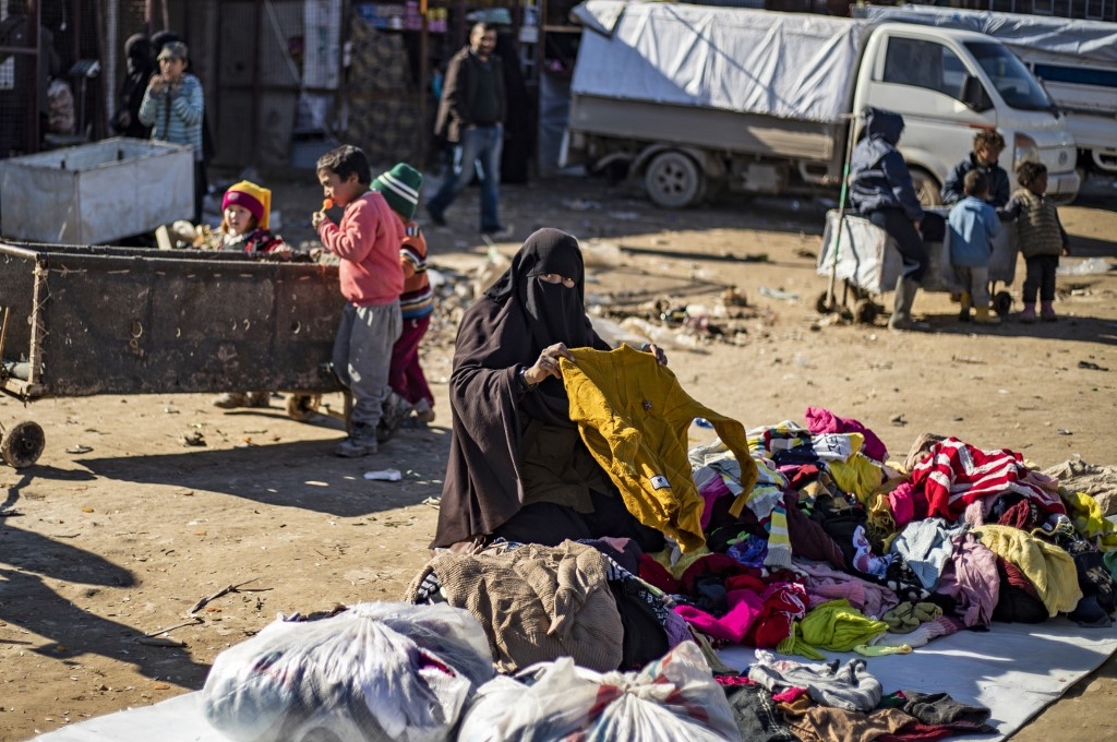 A woman sorts used clothing on the ground at the Kurdish-run al-Hol camp in northeastern Syria on 14 January (AFP/File photo) 