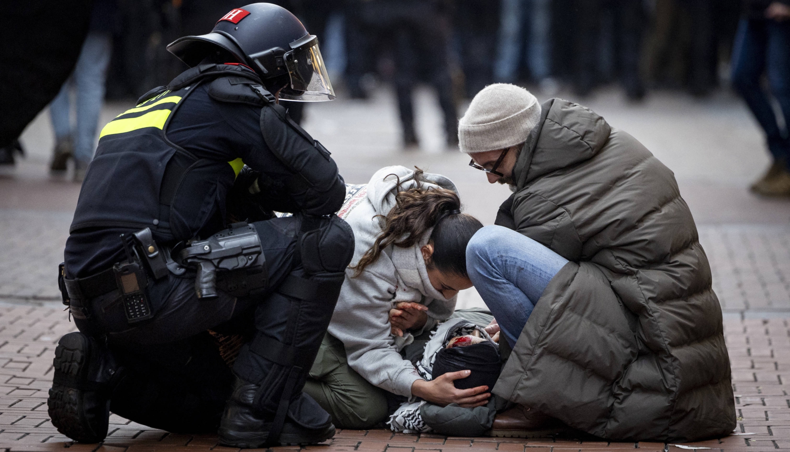 A police officer watches demonstrators helping a bloodied protester near Dam Square during a Pro-Palestine protest in Amsterdam on 10 November 2024 (AFP)