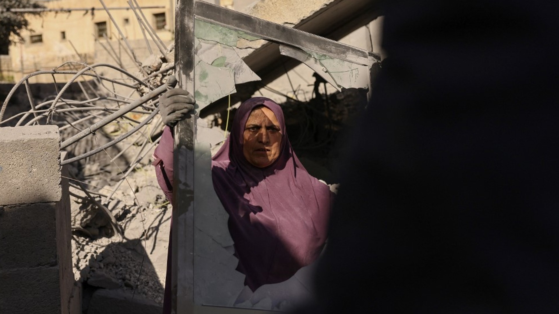 A woman holds a broken window amid the rubble of a demolished house in the village of Bani Naim, in the occupied West Bank on 17 April, 2024 (Hazem Bader/AFP)