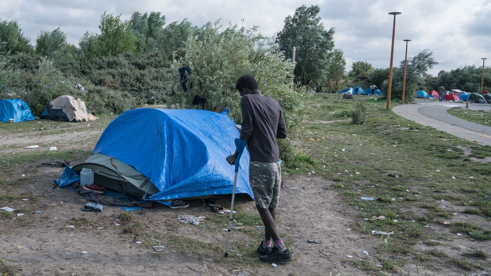 An injured man enroute to the UK walks towards a tent outside Calais, northern France (MEE/Abdul Saboor)