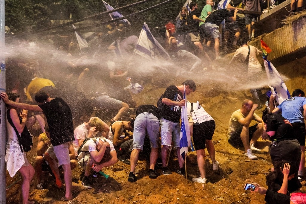 Demonstrators are sprayed by water cannon during a protest against the Israeli government's judicial overhaul plan, Tel Aviv, 8 July 2023 (AFP)
