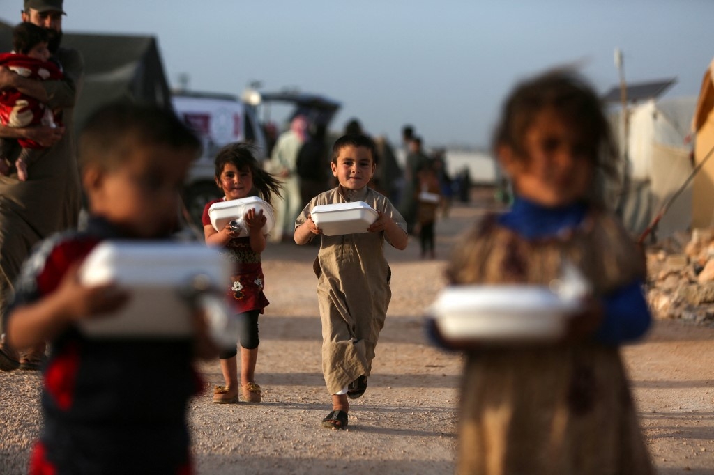 Displaced Syrian children with boxes of food distributed by a local charity, before the Iftar meal during Ramadan, at a camp for displaced people in Syria's northwestern Idlib province, 3 April 2022 (AFP)