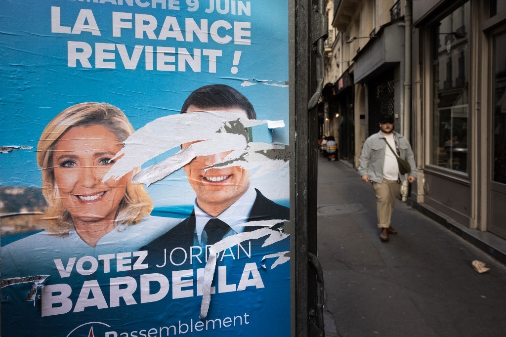 A man walks past an electoral poster of the National Rally (RN) with defaced portraits of party president Jordan Bardella (R) and leader of parliamentary group Marine Le Pen (L), in Paris on 10 June (Joel Saget/AFP)