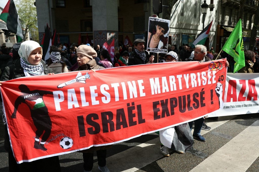 Demonstrators hold a banner reading “Martyrised Palestine, Israel expelled, JO [Olympic Games]” during a protest “against racism and Islamophobia” at the call of various organisations in Paris on 21 April (Alain Jocard/AFP)