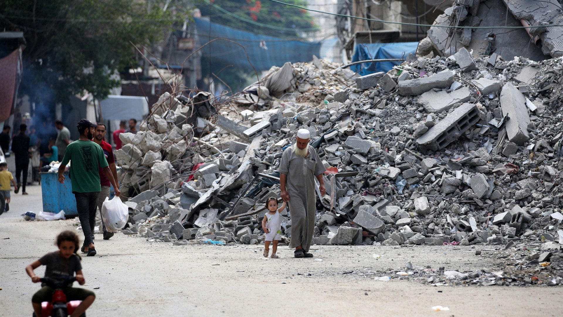 An elderly man holds a child by the hand as he walks past a building levelled by Israeli bombardment in the Bureij refugee camp in central Gaza Strip on 25 August (Eyad Baba/AFP)