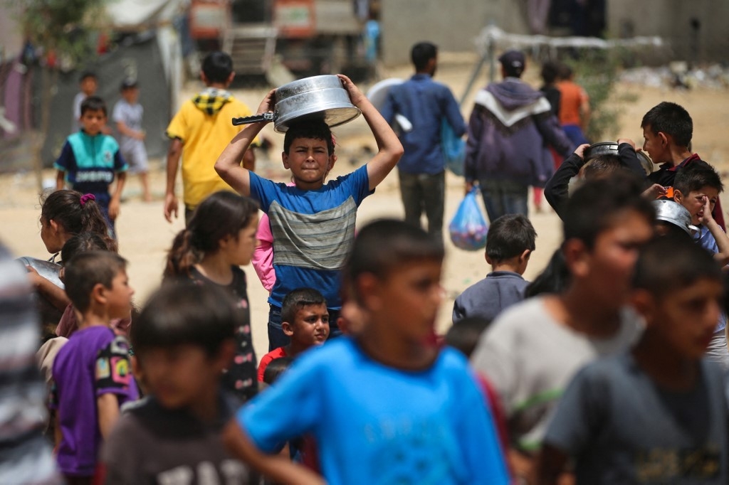 Displaced Palestinian children line up to receive food in Rafah on 19 May 2024 (AFP)