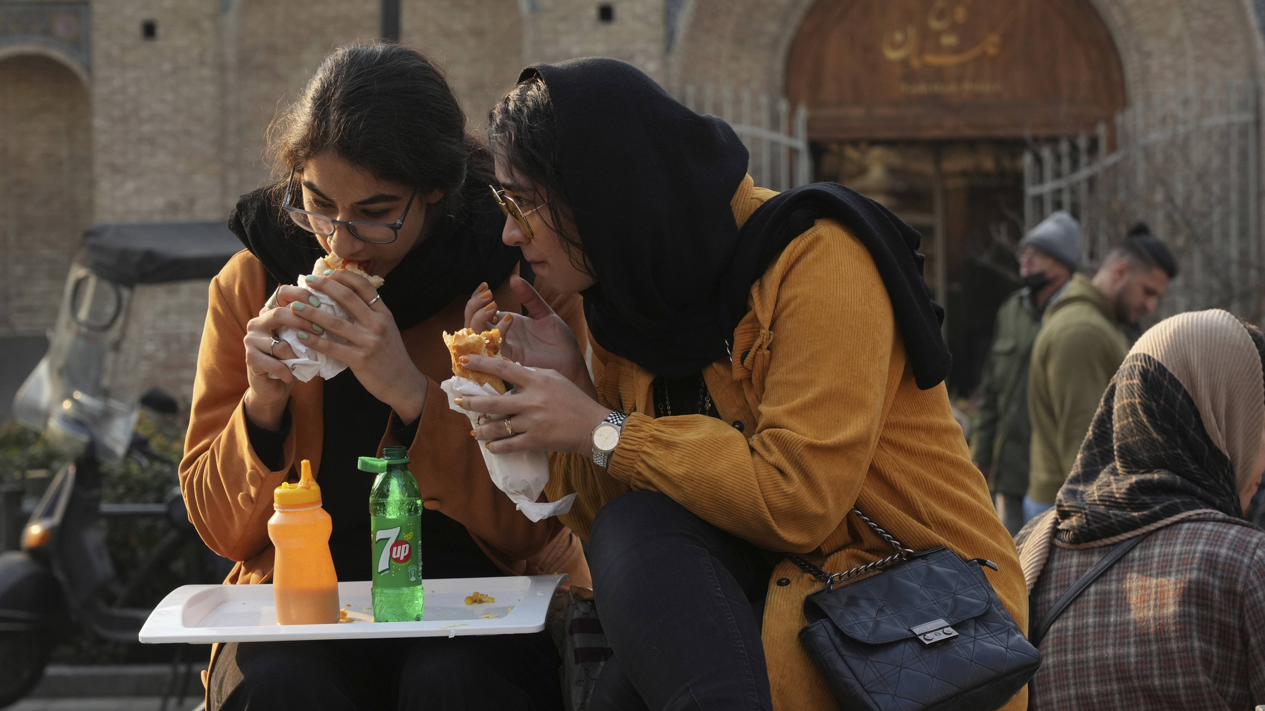 Two Iranian women eat sandwich in the outdoor area of a restaurant in downtown Tehran, 24 January 2023 (AP)