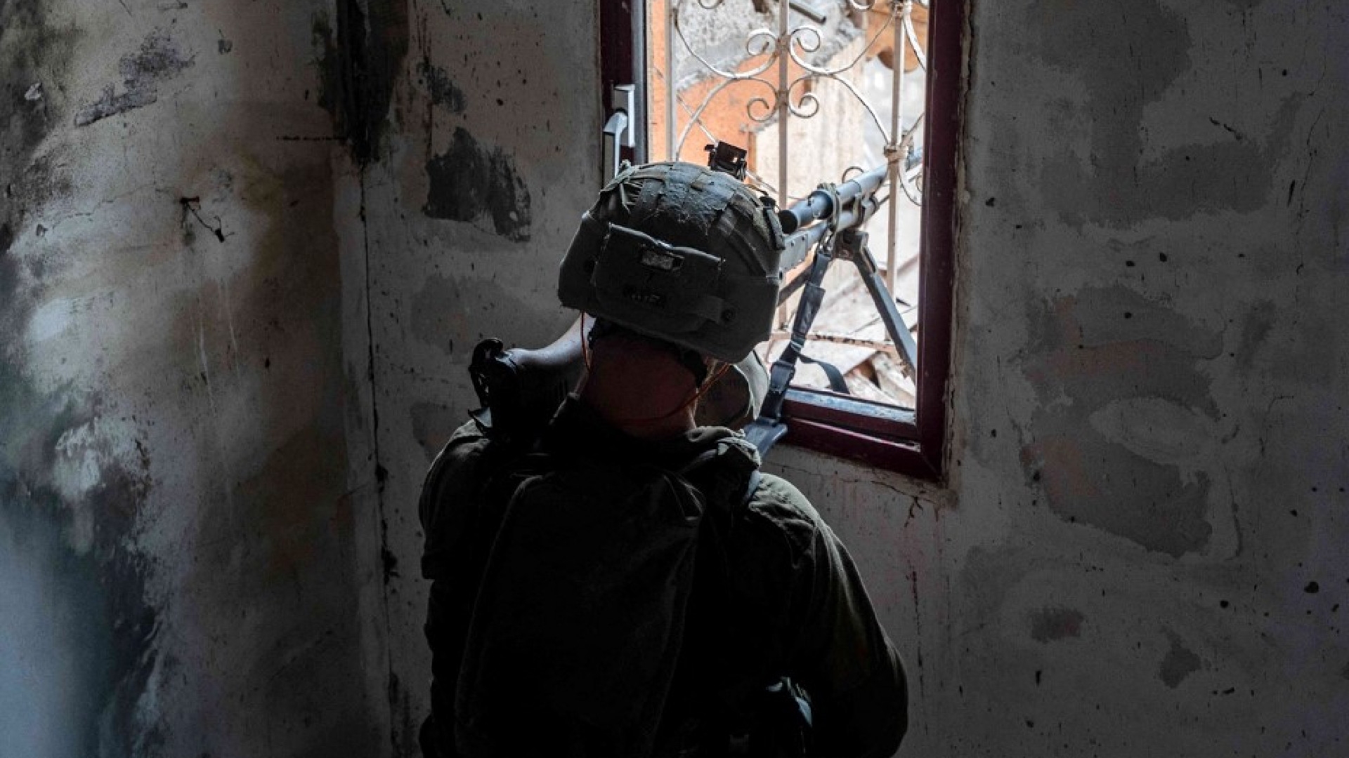 An Israeli soldier taking aim through a window during operations in the Gaza Strip, 6 June 2024 (AFP)