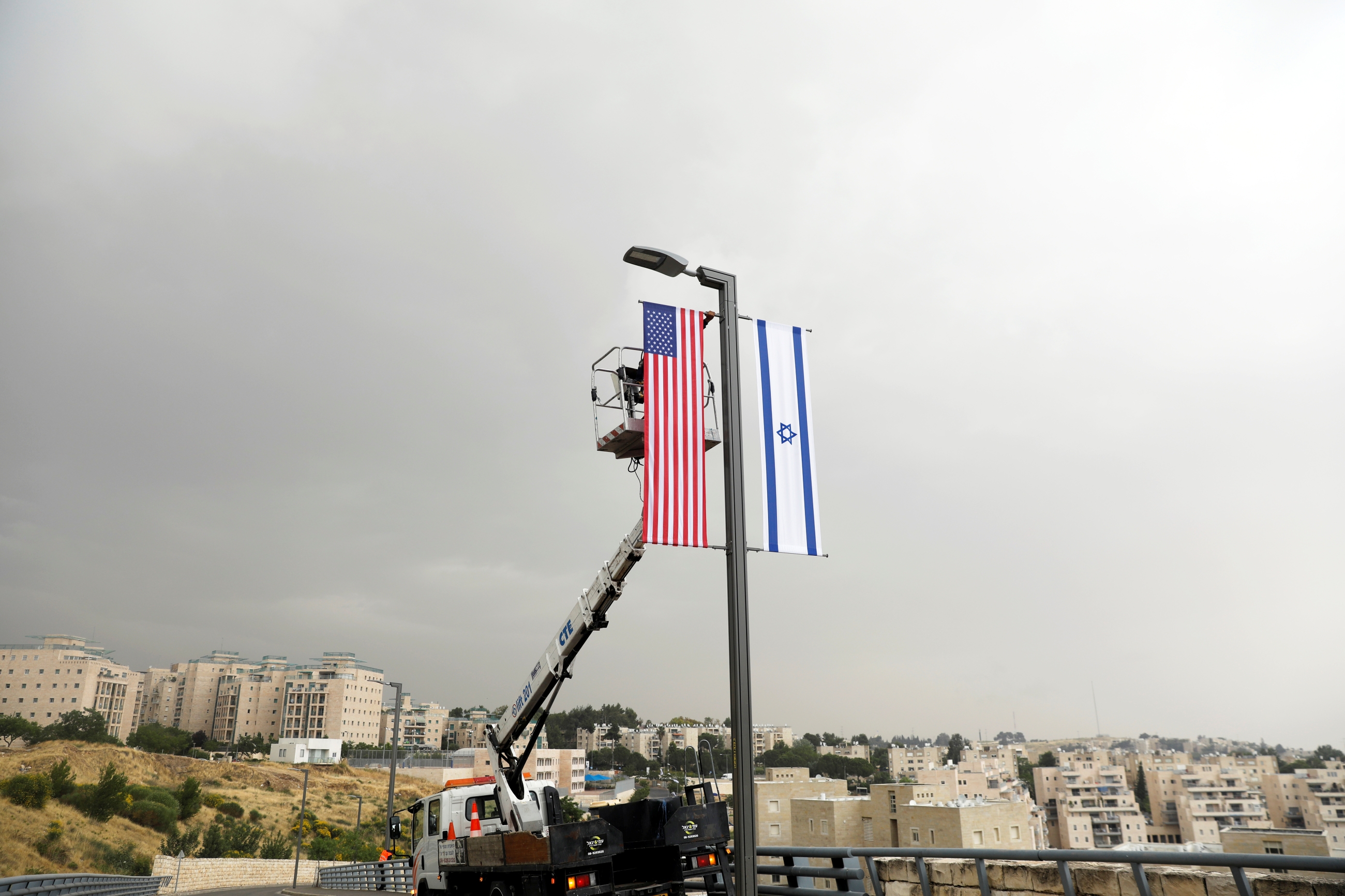 A worker on a crane hangs a US flag next to an Israeli flag, next to the entrance to the US consulate in Jerusalem on 7 May 2018 (Reuters)
