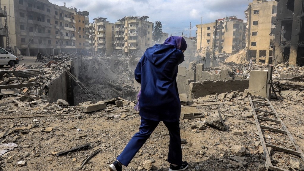 A woman walks past a crater where a building once stood following an overnight Israeli air strike on the neighbourhood of Kafaat in Beirut's southern suburbs earlier this month (AFP)