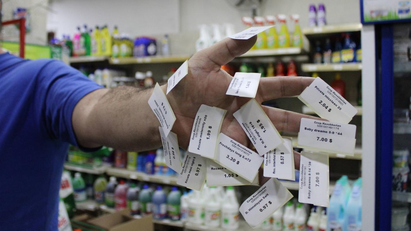 Razmig Keoshkerian découpe des étiquettes en dollars pour réétiqueter des articles de son magasin à Beyrouth, au Liban (MEE/Hanna Davis)
